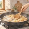 フライパンで凍ったチャーハンを木べらでほぐしながら温める様子